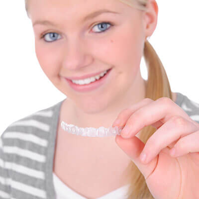 A young woman holding an Invisalign clear aligner