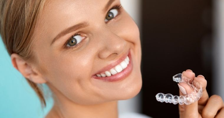 woman smiling and holding up her clear aligner