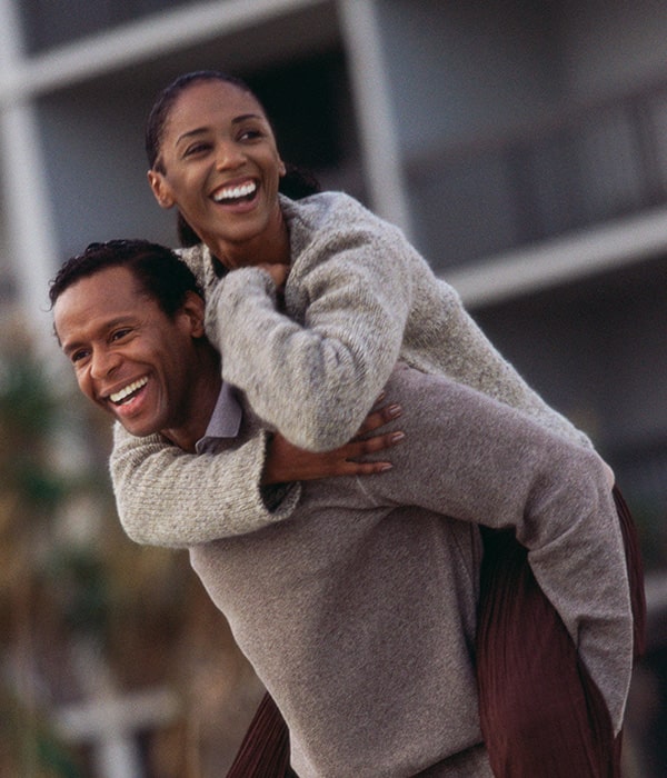 A woman riding piggyback on a man and smiling.